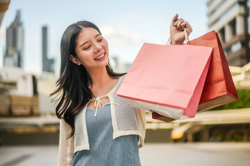 Portrait of Happy young shopaholic asian woman enjoying shopping weekend, holding packages bags and...
