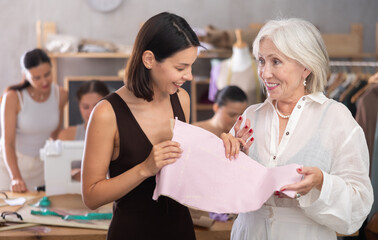 During sewing session, young female participant holding paper pattern pinned to fabric while...