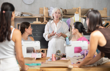 During practical sewing course for adults, mature female teacher using chalkboard to explain basic...