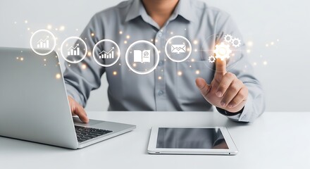 Man interacting with digital icons over laptop and tablet on a white desk in a bright office space