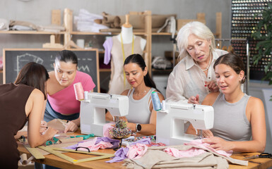Positive women sewing and preparing dress scheme together with instructor during tailor lesson