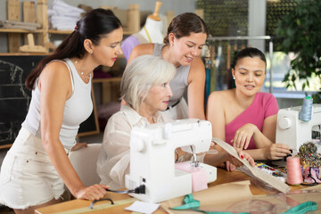 Friendly mature woman demonstrating sewing technique to others during sewing lesson