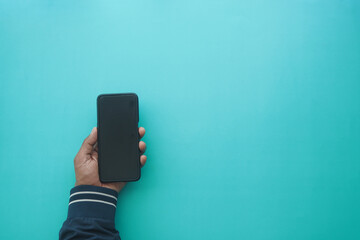 Hand holding smartphone on blue background at home
