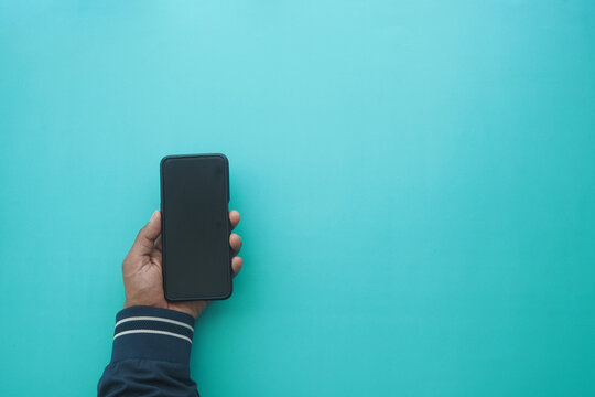 Hand holding smartphone on blue background at home - Powered by Adobe