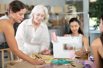 Young woman teacher shows group women how to draw pattern on paper at sewing master class