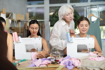 Group of women sewing on machine and draw pattern on paper during lesson at sewing workshop