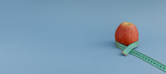 A red apple with a measuring tape on a blue background with space for text. Banner. The concept of...