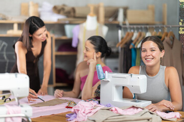 Group of women sewing on machine and attaching template to fabric at sewing workshop