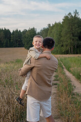 A happy dad with his son in his arms in a wheat field in summer. Family concept, father's role in the family