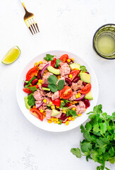 Mexican style salad with canned tuna, avocado, corn, red beans, cherry tomatoes and cilantro, white table background, top view
