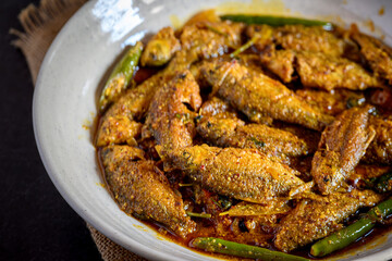 Bengali-style puti fish jhal served in a bowl – spicy small fish curry, traditional Bengali non-veg dish, puti macher jhal, Indian freshwater fish in mustard gravy, homestyle overhead view
