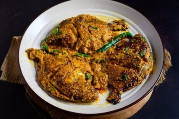 Pomfret jhal served in a plate – spicy Bengali pomfret curry, Indian fish in mustard and chili gravy, traditional seafood dish, homestyle non-veg meal, overhead view
