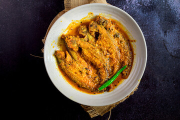 Bengali-style pabda fish in tomato-based red curry – pabda macher jhol, traditional Bengali fish dish, Indian freshwater fish curry, spicy homestyle fish preparation, overhead view
