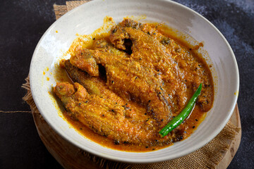 Bengali-style pabda fish in tomato-based red curry – pabda macher jhol, traditional Bengali fish dish, Indian freshwater fish curry, spicy homestyle fish preparation, overhead view
