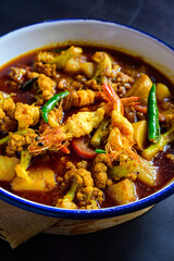Traditional Bengali-style prawn curry with potato and cauliflower garnished with green chillis – Indian seafood curry, authentic Bengali chingri recipe, homestyle jhol, rustic comfort food, top view