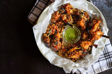 Korean-style baked chicken wings with sesame seeds served with green chilli sauce – Asian glazed chicken appetizer, spicy oven-baked wings, crispy Korean chicken, sesame garnish, food top view