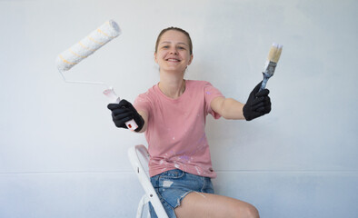 Young woman painting indoors wall with roller using stepladder