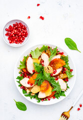 Autumn salad with grilled chicken, persimmon, pomegranate, walnuts, oranges and lettuce, top view
