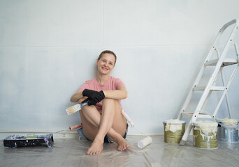 Young woman painting indoors wall with roller using stepladder
