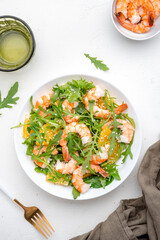 Seafood salad with juicy shrimps and orange, arugula and sesame on white background, top view