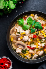 Chicken hot spicy soup with mushrooms, corn, white beans, chili pepper and cilantro. Black table background, top view