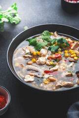 Chicken hot spicy soup with mushrooms, corn, white beans, chili pepper and cilantro. Black table background, top view