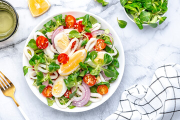 Seafood salad with squid, orange, tomatoes, lamb lettuce and olive oil with lemon juice dressing, gray table background, top view