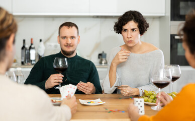 Two married couples are having fun in cozy home atmosphere, playing card game poker. Player makes lead move and believes in luck, emotionally waiting for victory, calculate winning combination