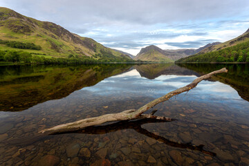 A peaceful landscape view of Buttermere Lake in the Lake District, UK, featuring calm water, clear...