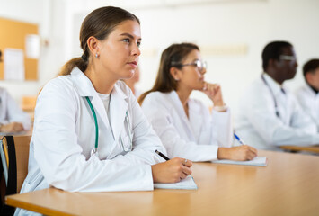 Girl medical student sitting at desk in classroom during lecture in medical college with group of...