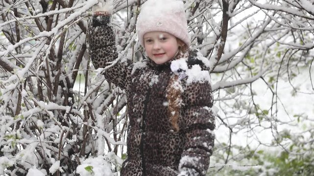 Cute little girl stretches her hand to catch falling snowflakes.