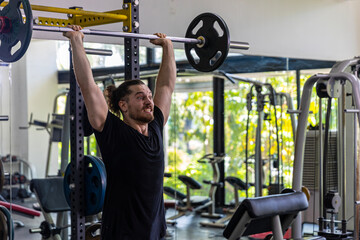 Good looking fitness trainer shows how to raise heavy barbell from squat racks with safety steps as part of body building exercise. A man using barbell to improve his physical power in a gym