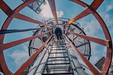 Male worker climbs up the ladder inspection column refinery work at height