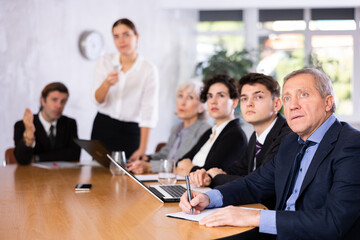 Woman and man sitting at table beside her colleagues during meeting in conference room