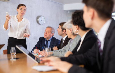 Woman and man sitting at table beside her colleagues during meeting in conference room