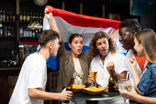 Fans with flag of Netherlands celebrate victory of their favorite team in a beer bar - Powered by Adobe