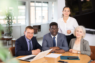 Group of different people in business suits pose sitting at table in office..
