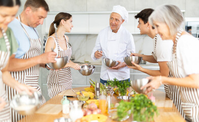 Friendly senior man, qualified chef, running culinary courses for mixed age group of ordinary passionate people, sharing professional secrets of cooking
