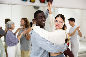Positive couple of dancers, engaged in a dance studio for adults, learns a slow foxtrot in lesson