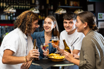 Two couples spending time in bar, having fun while drinking beer and talking.