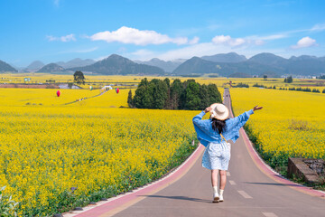 Obraz premium Young happy woman tourist enjoying the canola fields while traveling in Luoping, China