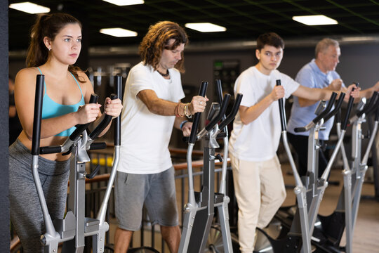 Group of athletic people of different ages train on elliptical trainers steppers