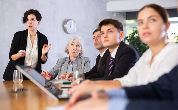 Focused young Latin American business woman presenting new business strategy to partners in office sitting at table, switching presentation slides with clicker
