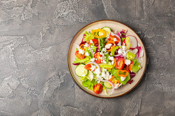 Cucumber salad on a wooden background.Homemade salad with fresh vegetables, cucumber, tomato, sweet pepper and lettuce in a plate.Vegetarian spring salad.Vegetarian diet.Healthy eating.Space for text