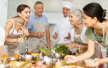 Positive friendly woman participating in group culinary masterclass led by professional chef,...