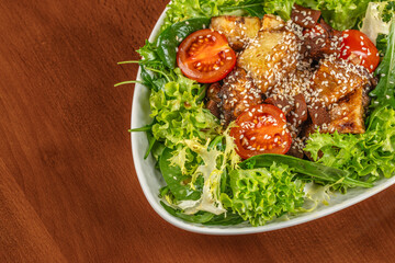 Fresh green salad with grilled eggplant, cherry tomatoes, and sesame seeds served in a white oval bowl on a wooden table