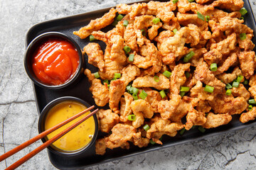 Little Crispy Pork or xiao su rou is a Sichuan dish of small strips of battered and fried pork closeup on the plate on the table. Horizontal top view from above