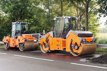 Road construction machinery parked. Two orange asphalt rollers. Freshly paved surface. Modern heavy...