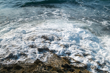 Sea waves crashing against rocky shore at Sardala Bay Kocaeli - dramatic white foam and splash on rugged coastal rocks under clear sunny weather conditions