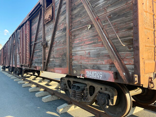 A weathered, rustic wooden freight train car on tracks under a clear sky, showcasing industrial...